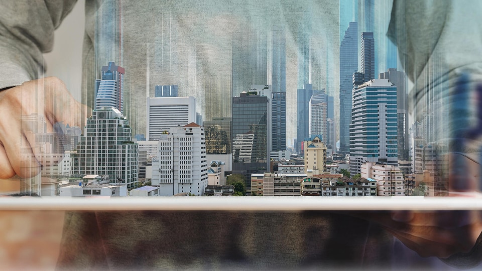 A person holds a tablet from which a semi-transparent city skyline with skyscrapers emerges, overlaid with vertical digital light streaks.